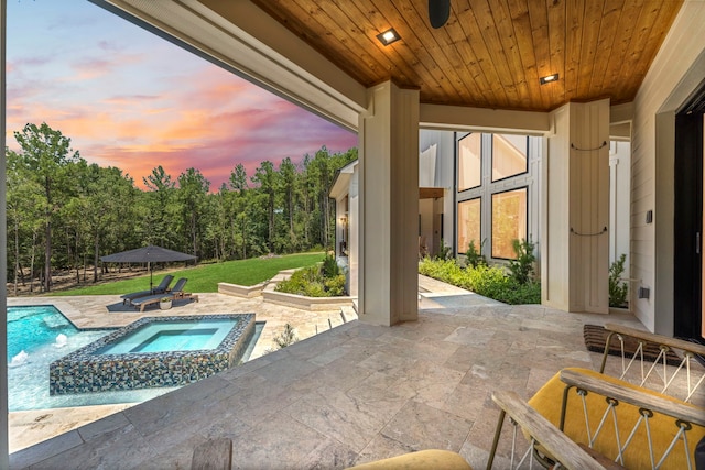 pool at dusk featuring an in ground hot tub and a patio area