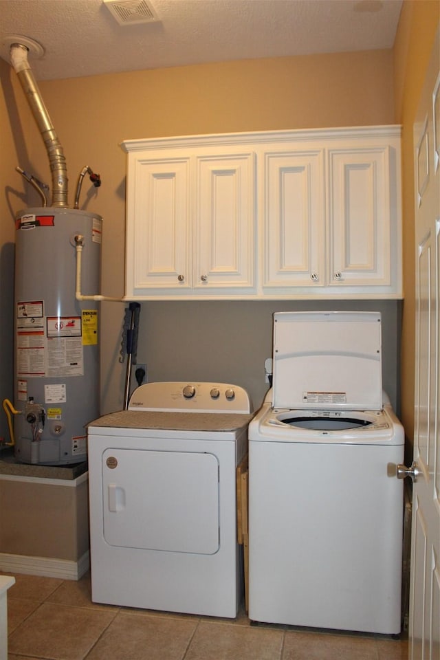 clothes washing area with washer and clothes dryer, light tile patterned flooring, cabinets, and water heater