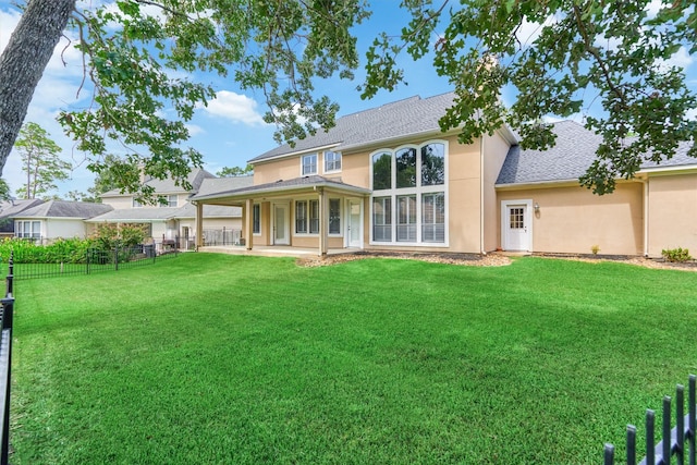 back of house with a shingled roof, stucco siding, a lawn, and fence