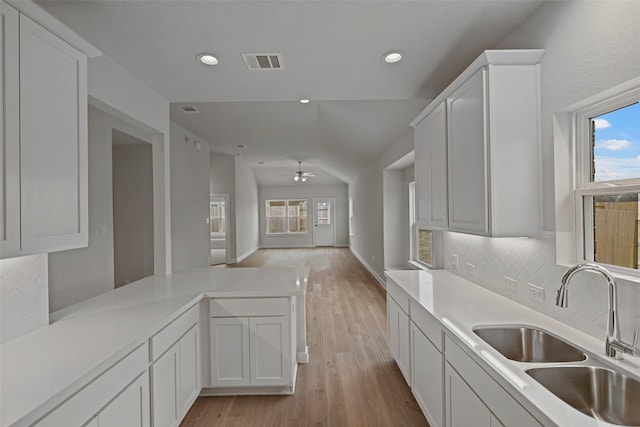 kitchen featuring tasteful backsplash, lofted ceiling, white cabinetry, light hardwood / wood-style flooring, and sink