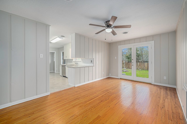 unfurnished living room featuring ceiling fan, light wood-type flooring, a textured ceiling, and french doors