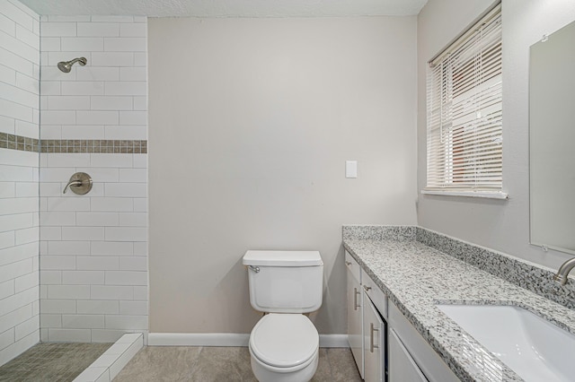 bathroom with a tile shower, vanity, a textured ceiling, and toilet