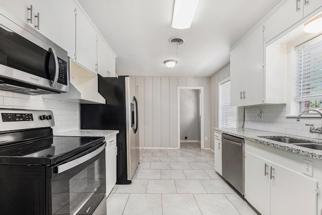 kitchen with appliances with stainless steel finishes, backsplash, sink, white cabinetry, and light tile patterned flooring