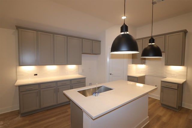 kitchen with an island with sink, gray cabinetry, dark wood-type flooring, hanging light fixtures, and sink