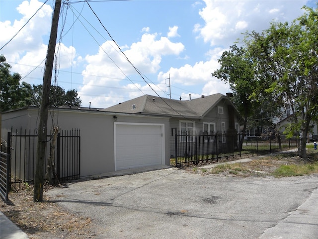 view of side of home featuring a garage, a fenced front yard, aphalt driveway, and stucco siding