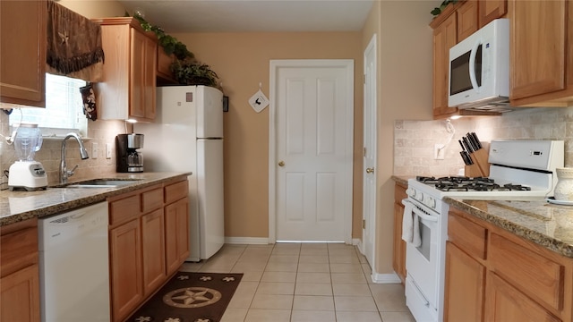 kitchen with light stone counters, backsplash, white appliances, light tile patterned floors, and sink