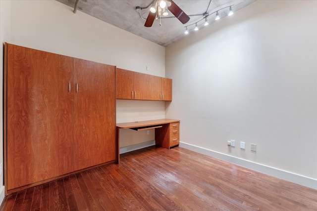 unfurnished office featuring dark hardwood / wood-style floors, ceiling fan, a high ceiling, rail lighting, and built in desk