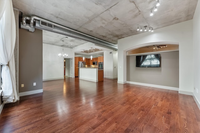 unfurnished living room with rail lighting, ceiling fan with notable chandelier, and wood-type flooring