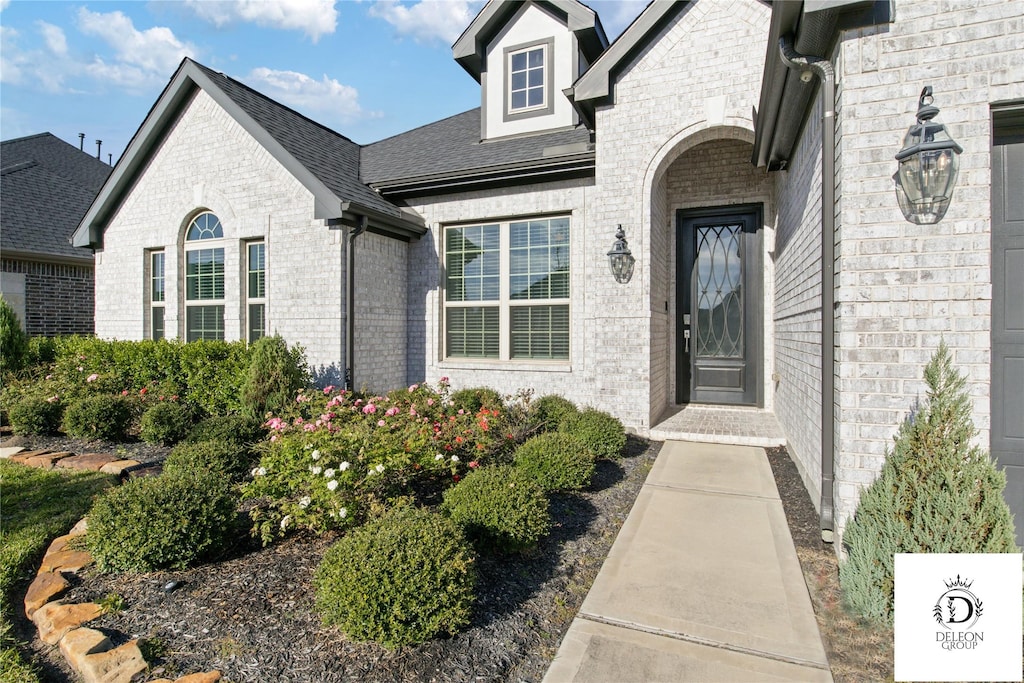 view of exterior entry featuring a shingled roof and brick siding