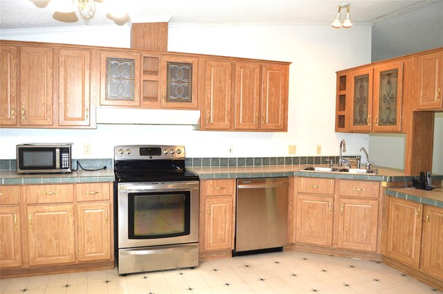 kitchen with vaulted ceiling, tile counters, stainless steel appliances, and sink