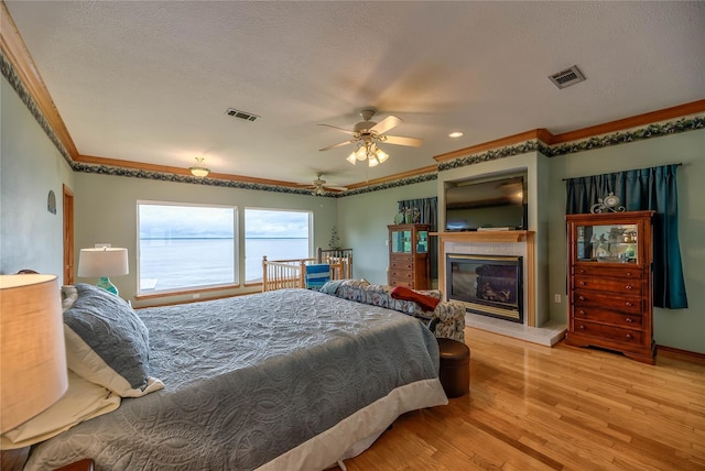 bedroom with a tile fireplace, ornamental molding, ceiling fan, light hardwood / wood-style floors, and a textured ceiling