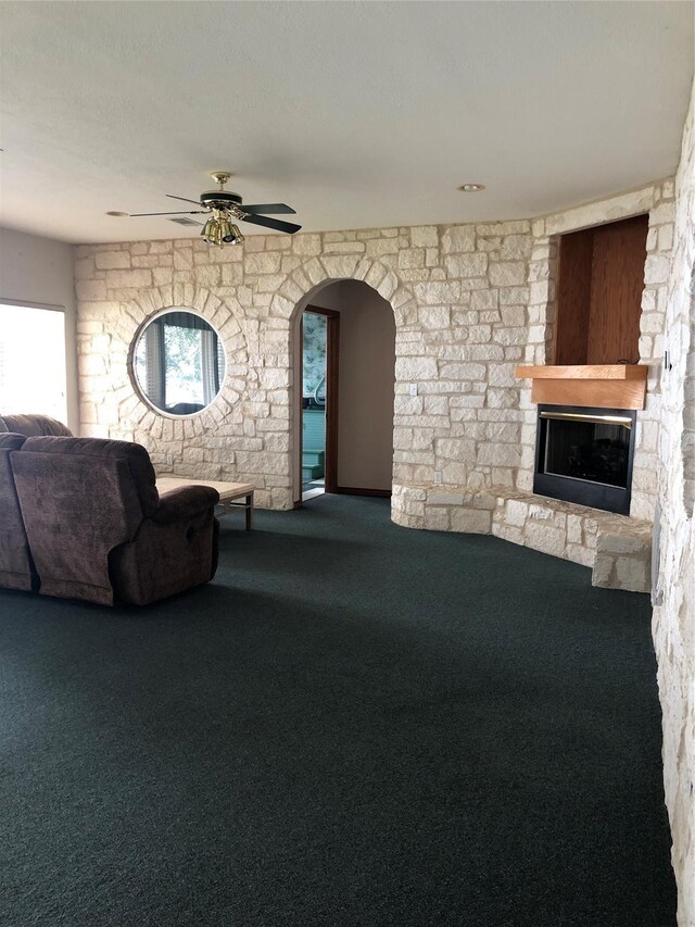 unfurnished living room with ceiling fan, a stone fireplace, and carpet