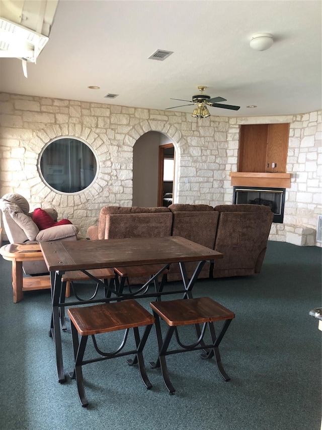 dining area featuring a stone fireplace, ceiling fan, and carpet