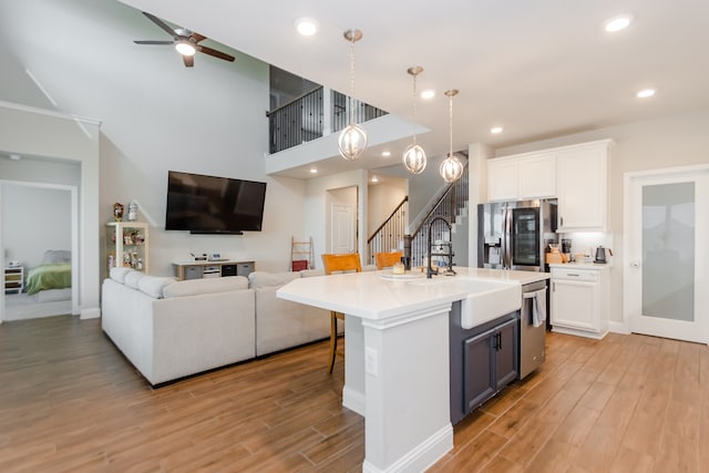 kitchen with stainless steel appliances, decorative light fixtures, a center island with sink, and light hardwood / wood-style floors