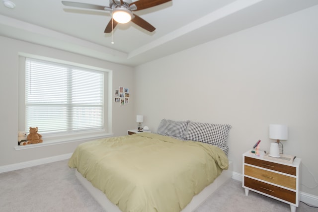 carpeted bedroom featuring ceiling fan, a tray ceiling, and multiple windows