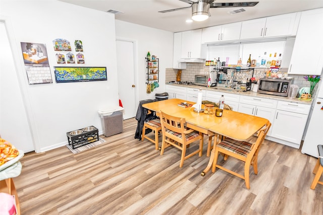 kitchen with white cabinets, light wood-type flooring, tasteful backsplash, and ceiling fan