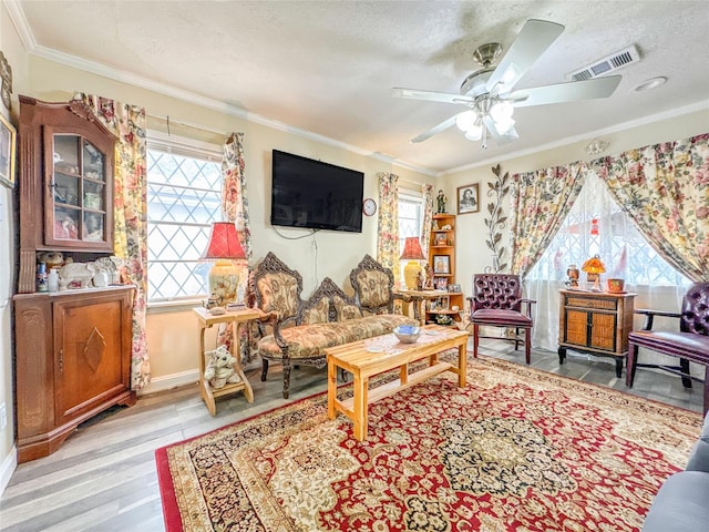 interior space featuring a textured ceiling, a ceiling fan, light wood-style floors, visible vents, and crown molding