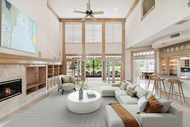 living room with french doors, ornamental molding, ceiling fan, a high ceiling, and a tiled fireplace