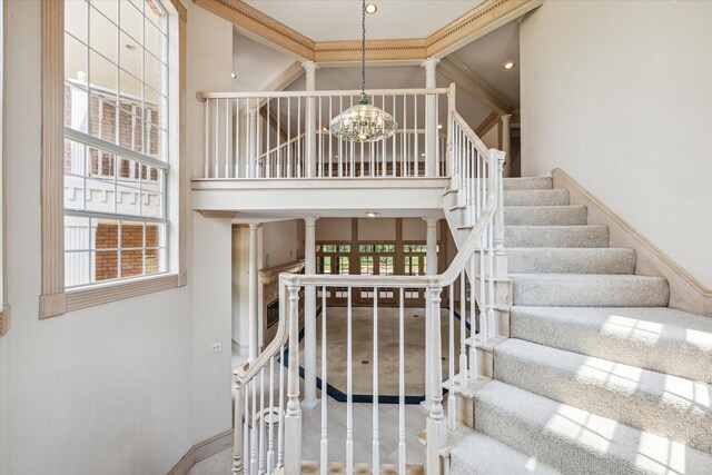 staircase with a high ceiling, decorative columns, crown molding, carpet floors, and a chandelier