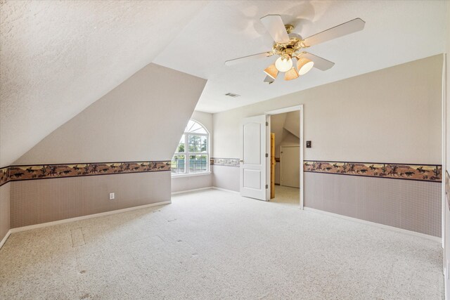 additional living space with lofted ceiling, ceiling fan, light colored carpet, and a textured ceiling