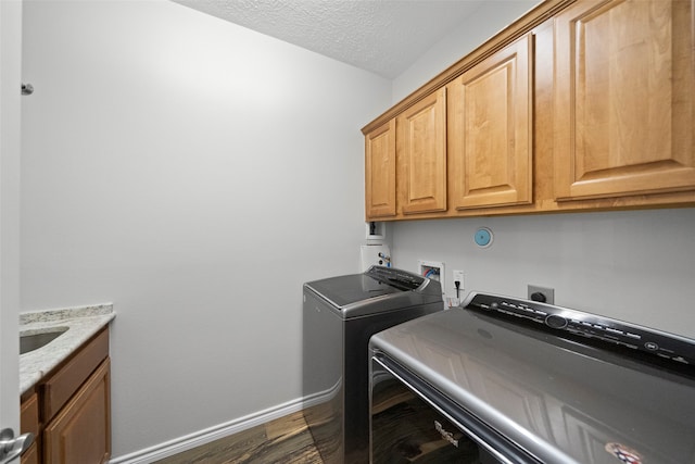 laundry area with a textured ceiling, washing machine and dryer, cabinets, and dark hardwood / wood-style floors