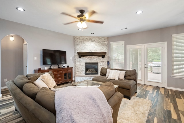 living room featuring ceiling fan, hardwood / wood-style flooring, a stone fireplace, and french doors