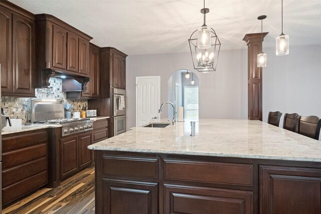 kitchen featuring backsplash, dark wood-type flooring, light stone counters, sink, and a center island with sink