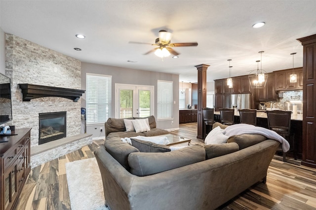 living room with ceiling fan, a stone fireplace, light hardwood / wood-style flooring, and french doors