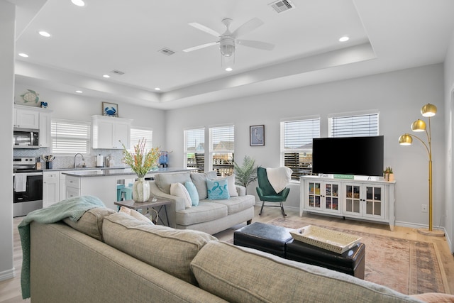 living room with light hardwood / wood-style flooring, a tray ceiling, sink, and ceiling fan