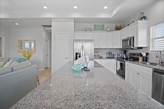 kitchen featuring appliances with stainless steel finishes, light hardwood / wood-style floors, sink, white cabinets, and decorative backsplash