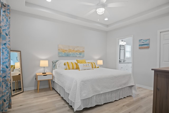 bedroom with a raised ceiling, ceiling fan, sink, connected bathroom, and light hardwood / wood-style flooring