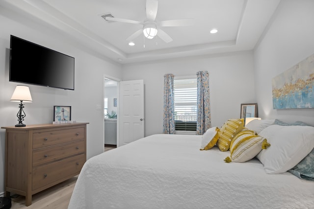 bedroom with a tray ceiling, ceiling fan, and light wood-type flooring