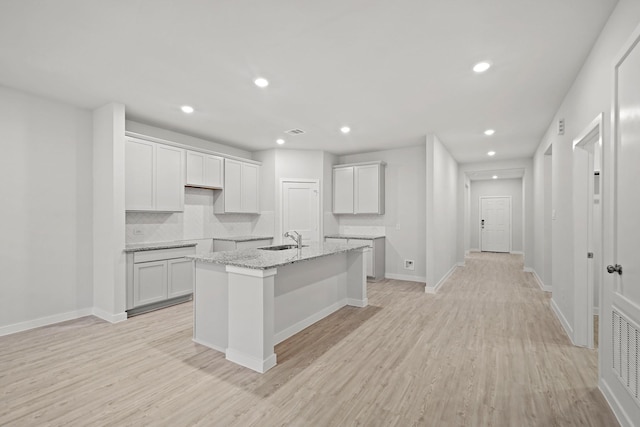 kitchen featuring tasteful backsplash, light stone counters, sink, white cabinets, and an island with sink