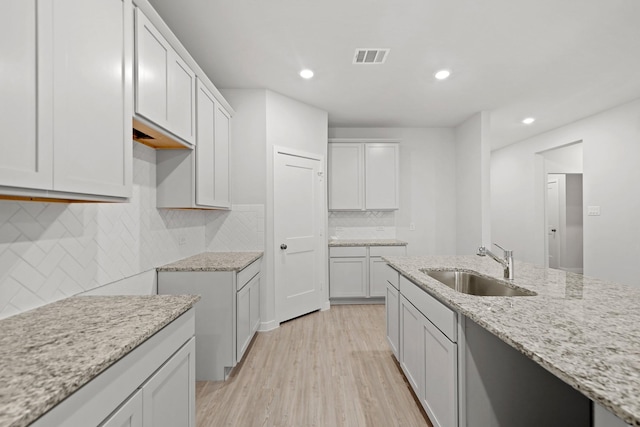 kitchen featuring backsplash, white cabinets, sink, light hardwood / wood-style flooring, and light stone counters