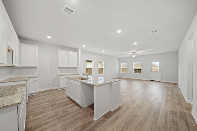 kitchen with white cabinets, light wood-type flooring, light stone counters, and a kitchen island with sink