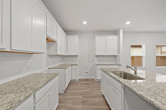 kitchen featuring light stone countertops, backsplash, sink, light hardwood / wood-style floors, and white cabinetry