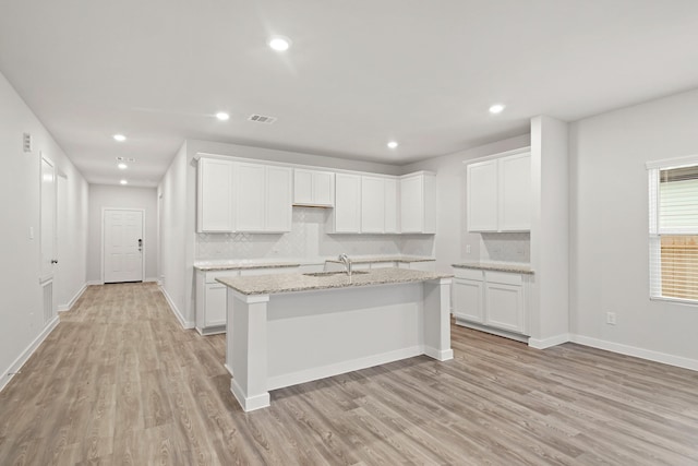 kitchen with decorative backsplash, light stone countertops, a kitchen island with sink, sink, and white cabinets