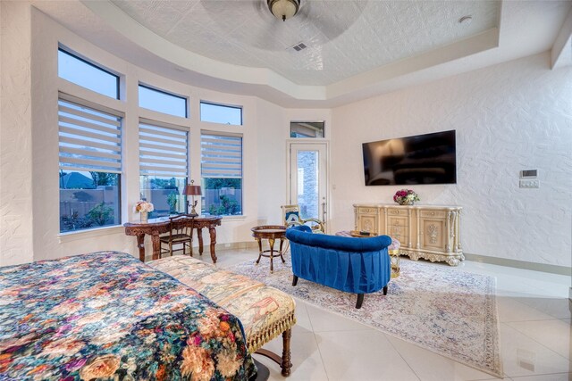 tiled bedroom featuring a textured ceiling, ceiling fan, and a raised ceiling