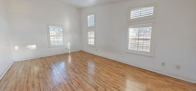 spare room with plenty of natural light, a towering ceiling, and light hardwood / wood-style flooring