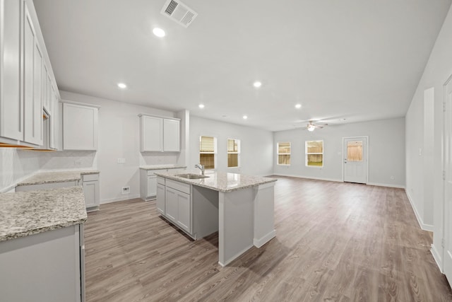 kitchen with sink, tasteful backsplash, white cabinetry, and an island with sink