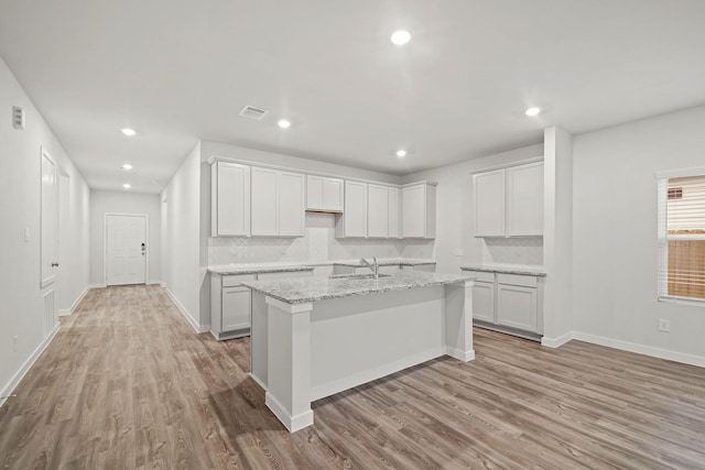 kitchen featuring backsplash, a kitchen island with sink, sink, light hardwood / wood-style floors, and light stone counters