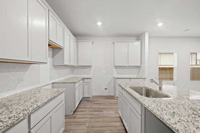 kitchen featuring sink, light wood-type flooring, tasteful backsplash, light stone counters, and white cabinetry