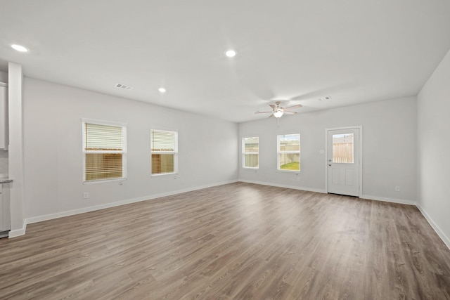 unfurnished living room with light wood-type flooring, a wealth of natural light, and ceiling fan