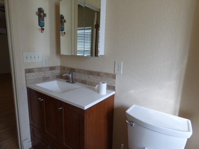 half bath featuring toilet, backsplash, and vanity