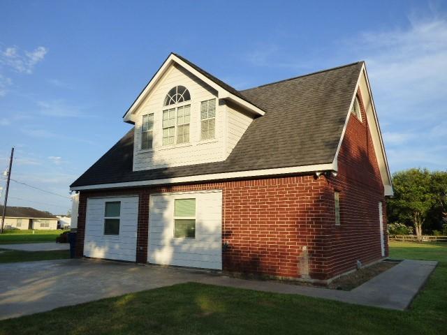 exterior space with brick siding, a yard, and roof with shingles