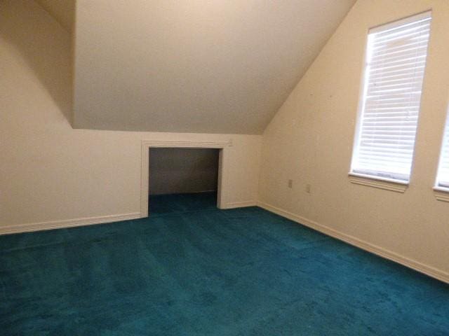 bonus room featuring dark colored carpet, vaulted ceiling, and baseboards