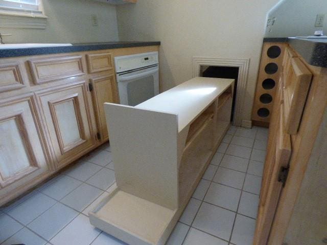 kitchen featuring white oven, dark countertops, light tile patterned flooring, a sink, and a peninsula