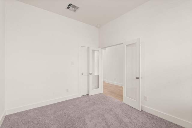 spare room with baseboards, visible vents, french doors, and light colored carpet