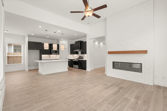 kitchen featuring open floor plan, appliances with stainless steel finishes, an island with sink, and dark cabinetry