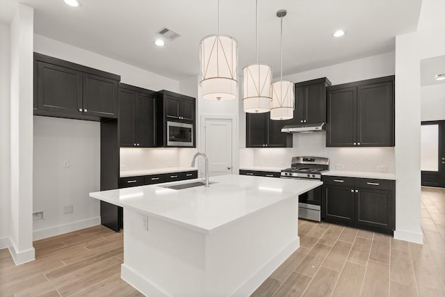 kitchen featuring visible vents, appliances with stainless steel finishes, a kitchen island with sink, light countertops, and dark cabinetry